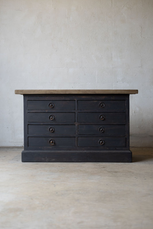 Dark wooden sideboard with drawers and a light wood countertop against a white wall.