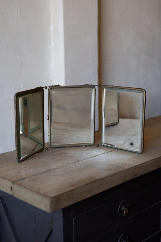 Vintage three panel barber mirror on a wooden surface with a neutral background