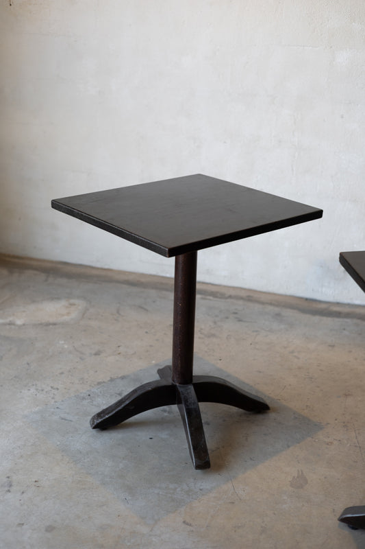 Small black bistro table with a single pedestal base on a concrete floor against a plain wall.