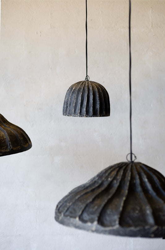 Three rustic papier mache pendant lights hanging against a plain wall.