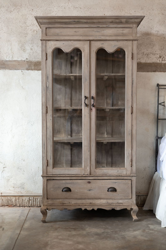 Vintage wooden cabinet with glass doors in a rustic room setting.