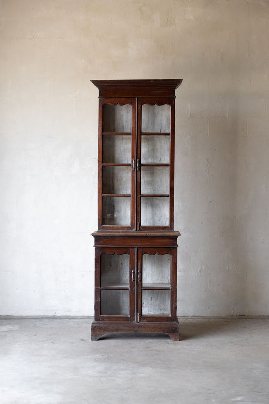 Wooden bookshelf with glass doors against a plain wall.