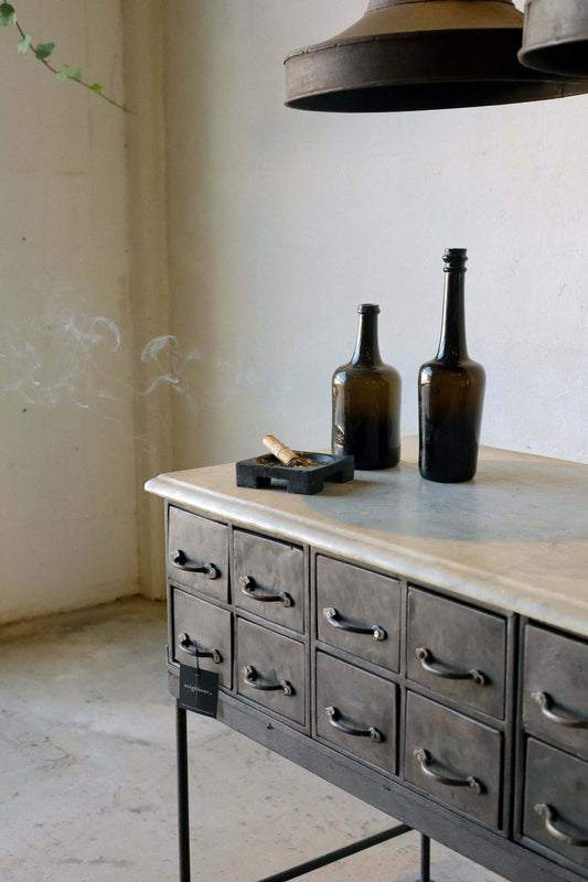 A square cast iron cigar tray on a marble-top console.