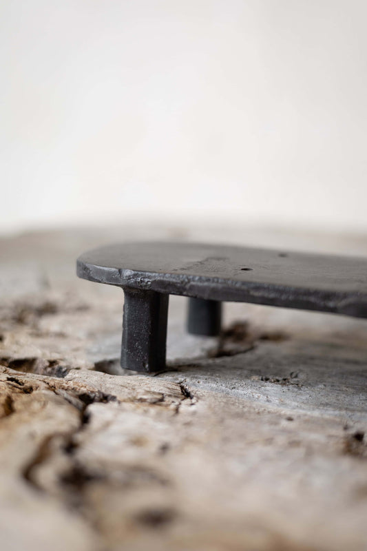 A black, oval cast iron soap stand on a worn wooden surface.