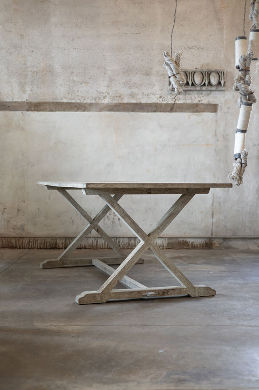 Wooden dining table with X-shaped base in a rustic interior setting