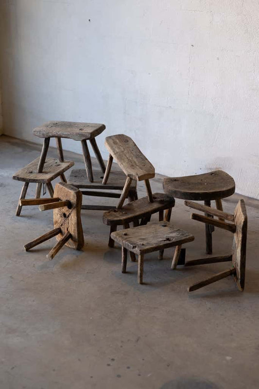 A pile of rustic, small, wooden stools with four legs. The stools are made out of old chopping blocks and logs.