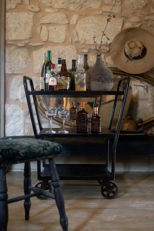 Iron bar cart with collection of spirits and glasses.