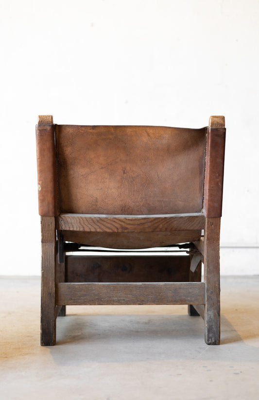 Back of vintage brown leather sling chair with wooden frame on a white background.