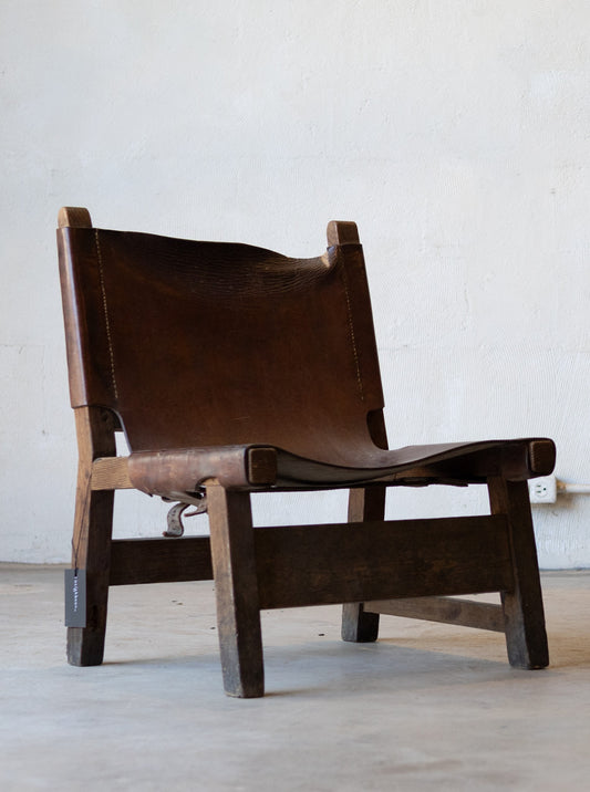 Vintage brown leather sling chair on a light wooden floor with a white wall background