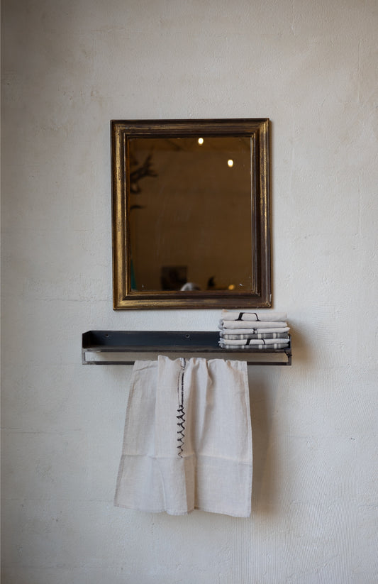 Compact metal shelf with with folded and hanging linens and a mirror on a textured wall