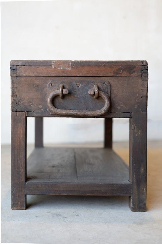 Side of vintage teak wood coffee table with an iron handle on a neutral background.