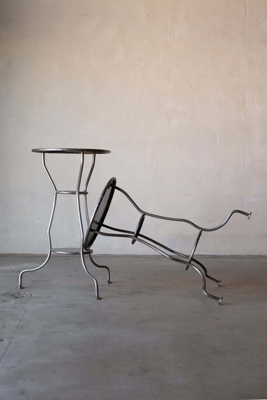 Two iron side tables with circular tops and three curved legs, one table leaning against the other.