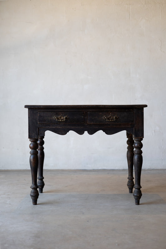 Dark wooden colonial vintage desk with decorative turned legs against a plain white wall.