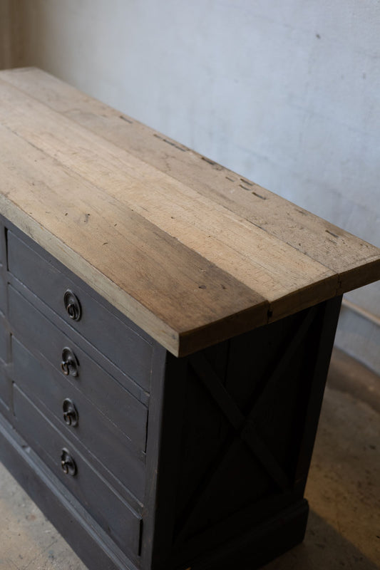 Dark wooden sideboard with drawers and a light wood countertop against a white wall.
