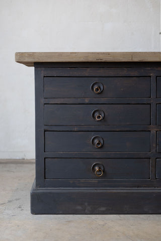 Dark wooden sideboard with drawers and a light wood countertop against a white wall.