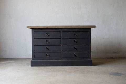 Dark wooden sideboard with multiple drawers against a plain wall.