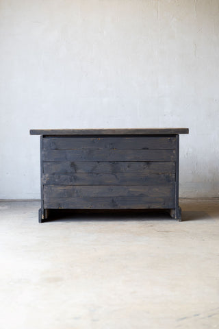 Rear view of wooden sideboard with drawers and a light wood countertop against a white wall.