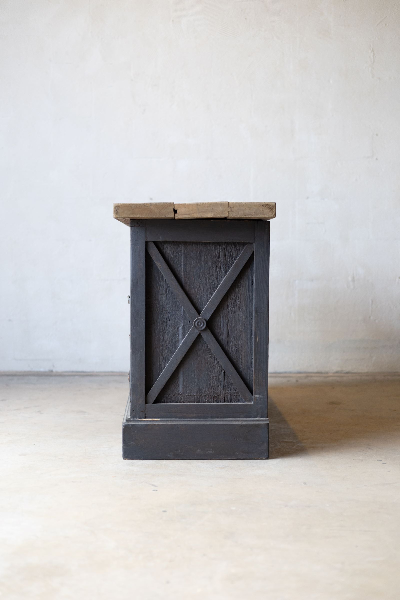 Side view of dark wooden sideboard with drawers and a light wood countertop against a white wall.