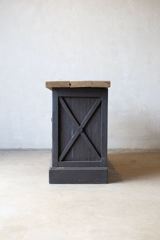 Side view of dark wooden sideboard with drawers and a light wood countertop against a white wall.