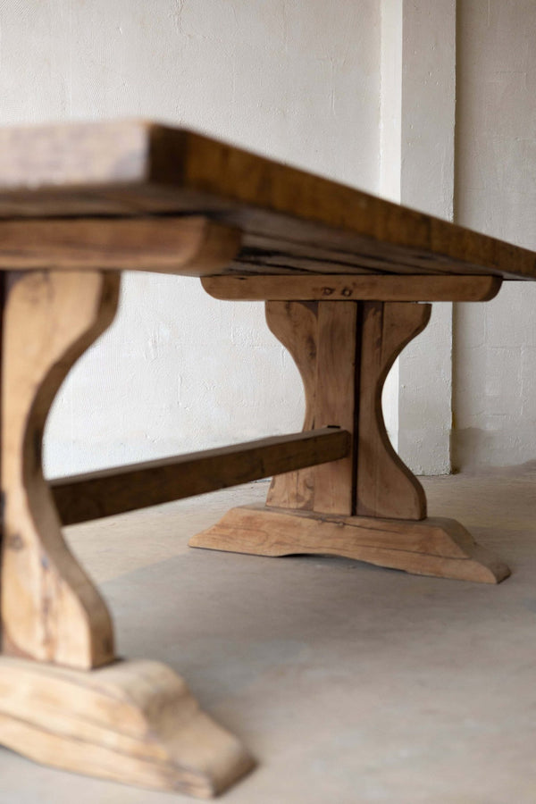 Wooden dining table with a thick tabletop and a sturdy trestle base featuring curved legs and a horizontal support beam. 