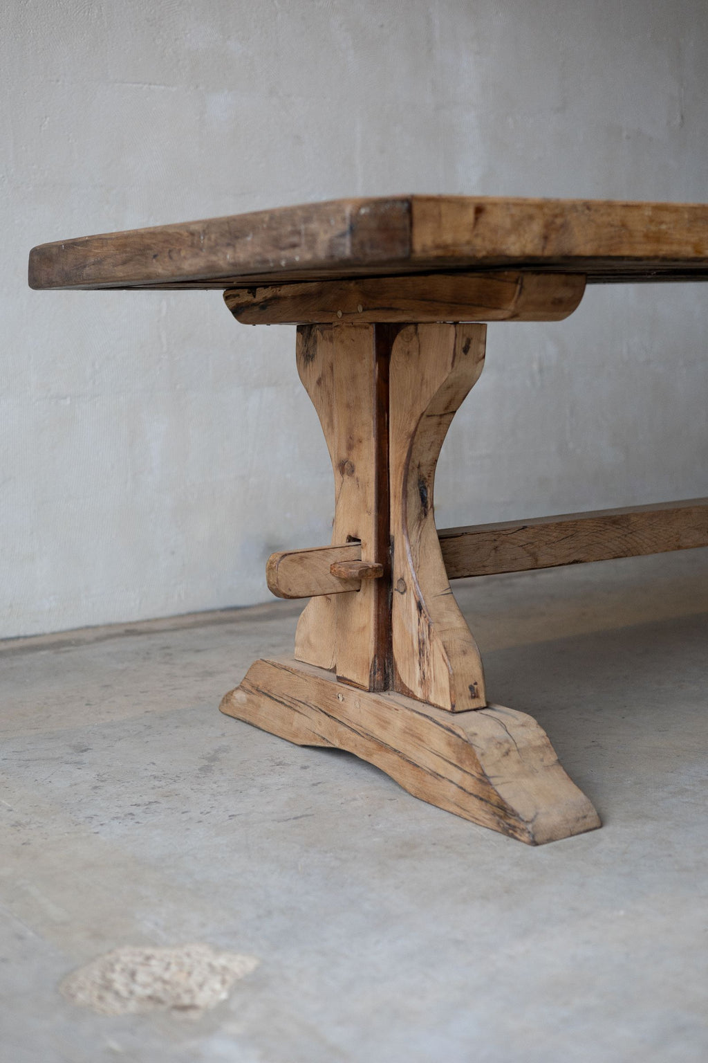 View of one end of wooden dining and natural, warm-toned grain. Features trestle base, curved leg, and horizontal support beam.