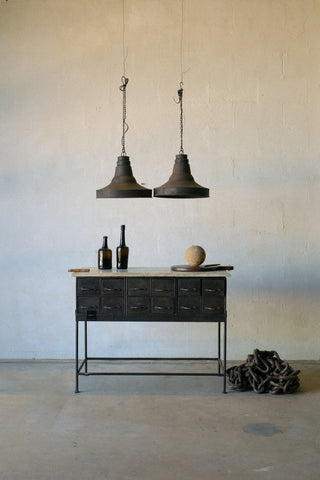 Zoomed out image of pair of pendant lights in industrial style, featuring natural patina, hanging over a small desk.