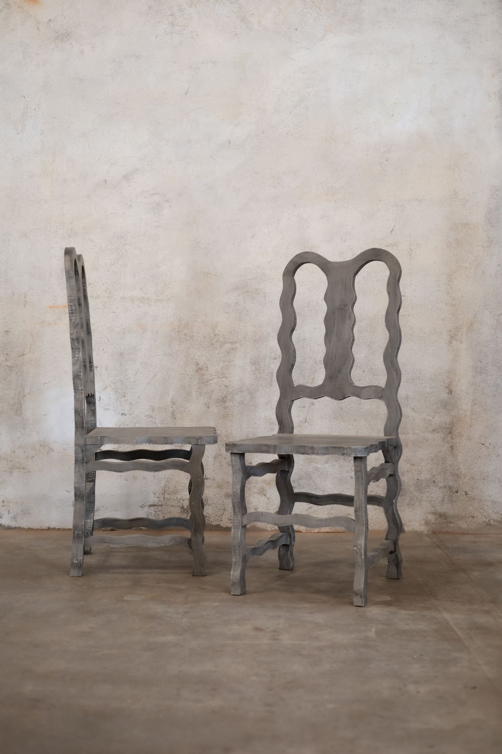 Two decorative wooden chairs against a textured wall.