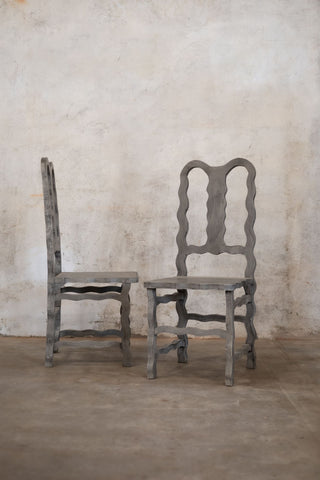 Two decorative wooden chairs against a textured wall.