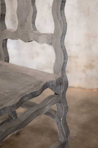 Decorative chair with wavy wooden frame and wooden seat against a textured wall.