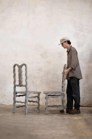 Person inspecting two vintage chairs against a plain wall.