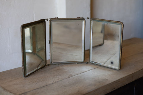 Vintage-style trifold mirror on a wooden surface with a white wall background
