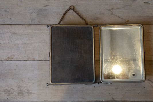 Vintage three panel barber mirror folded on a wooden surface with a neutral background