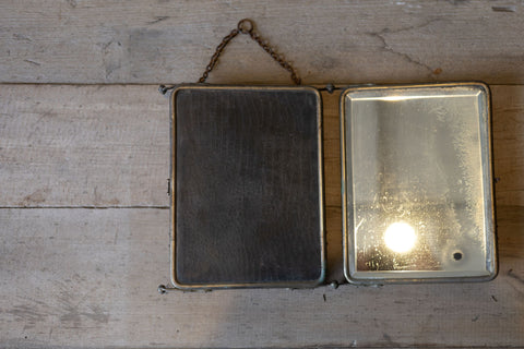 Vintage three panel barber mirror folded on a wooden surface with a neutral background