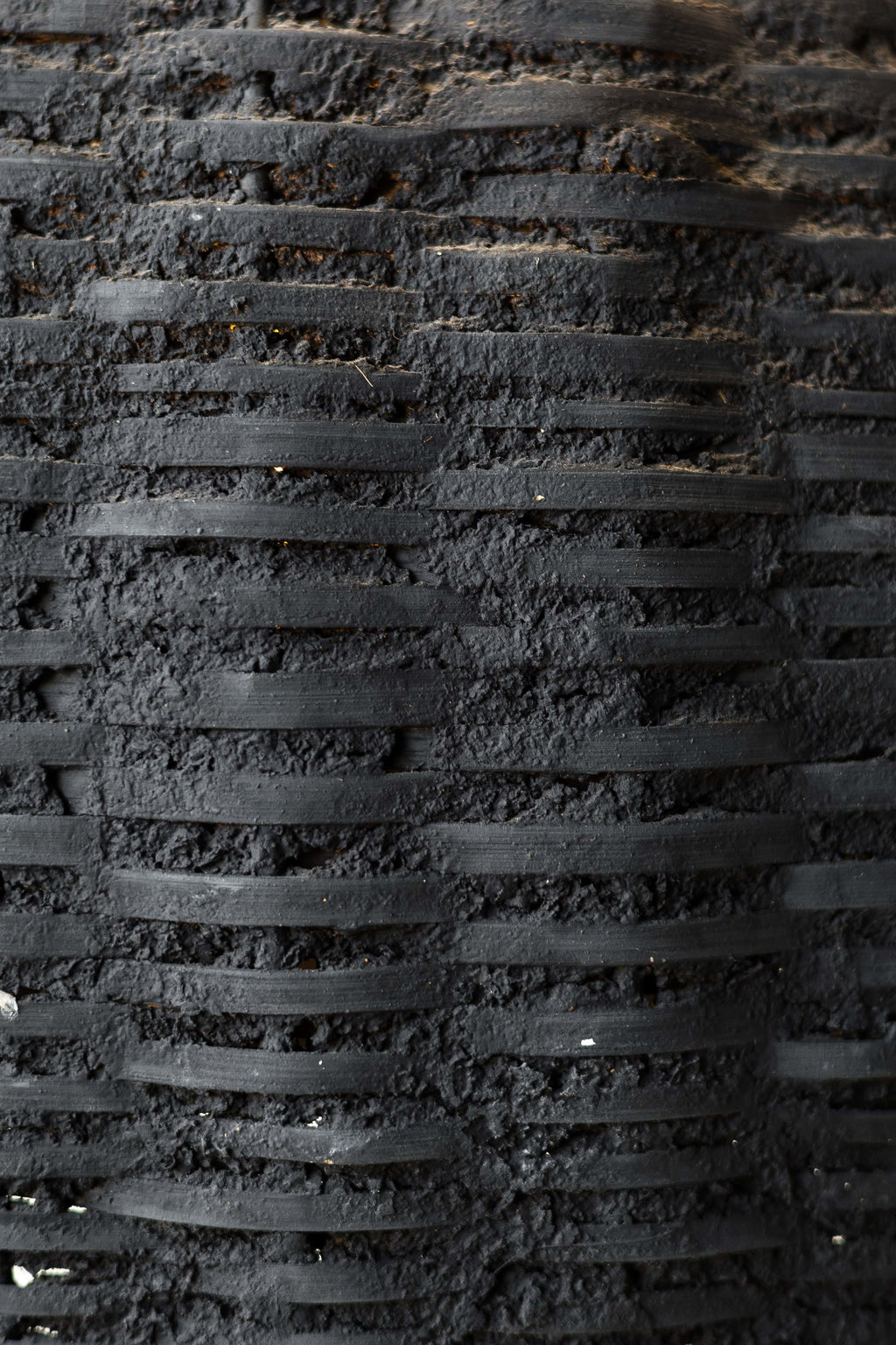 Close up of black woven beehive pendant showing the rustic texture of the clay and woven fibers.