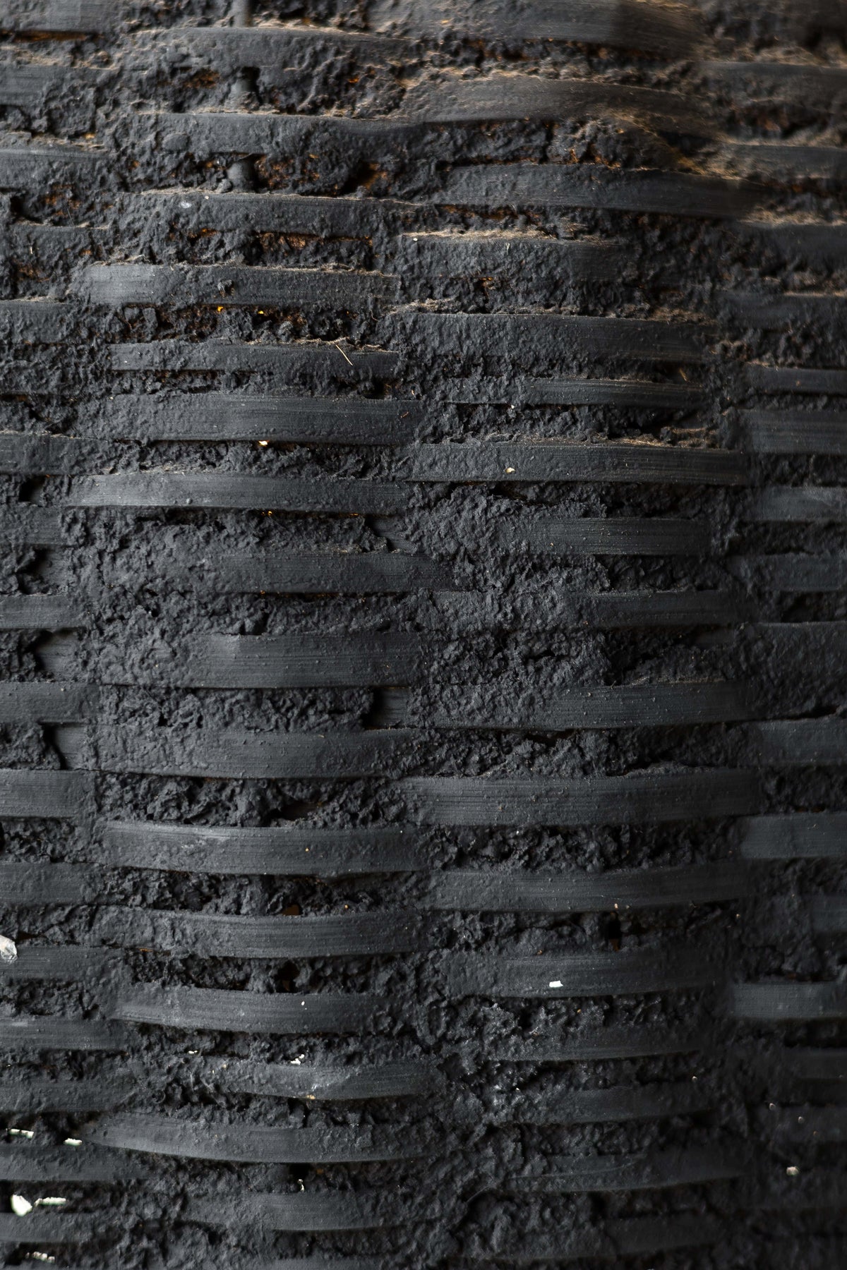 Close up of black woven beehive pendant showing the rustic texture of the clay and woven fibers.