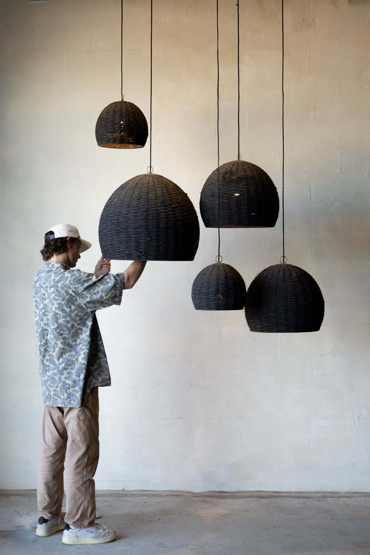 Group of five beehive pendant lights hanging at different heights with different sizes with man changing the light on one.  