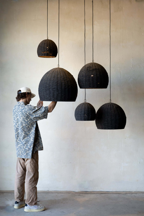 Group of five beehive pendant lights hanging at different heights with different sizes with man changing the light on one.  