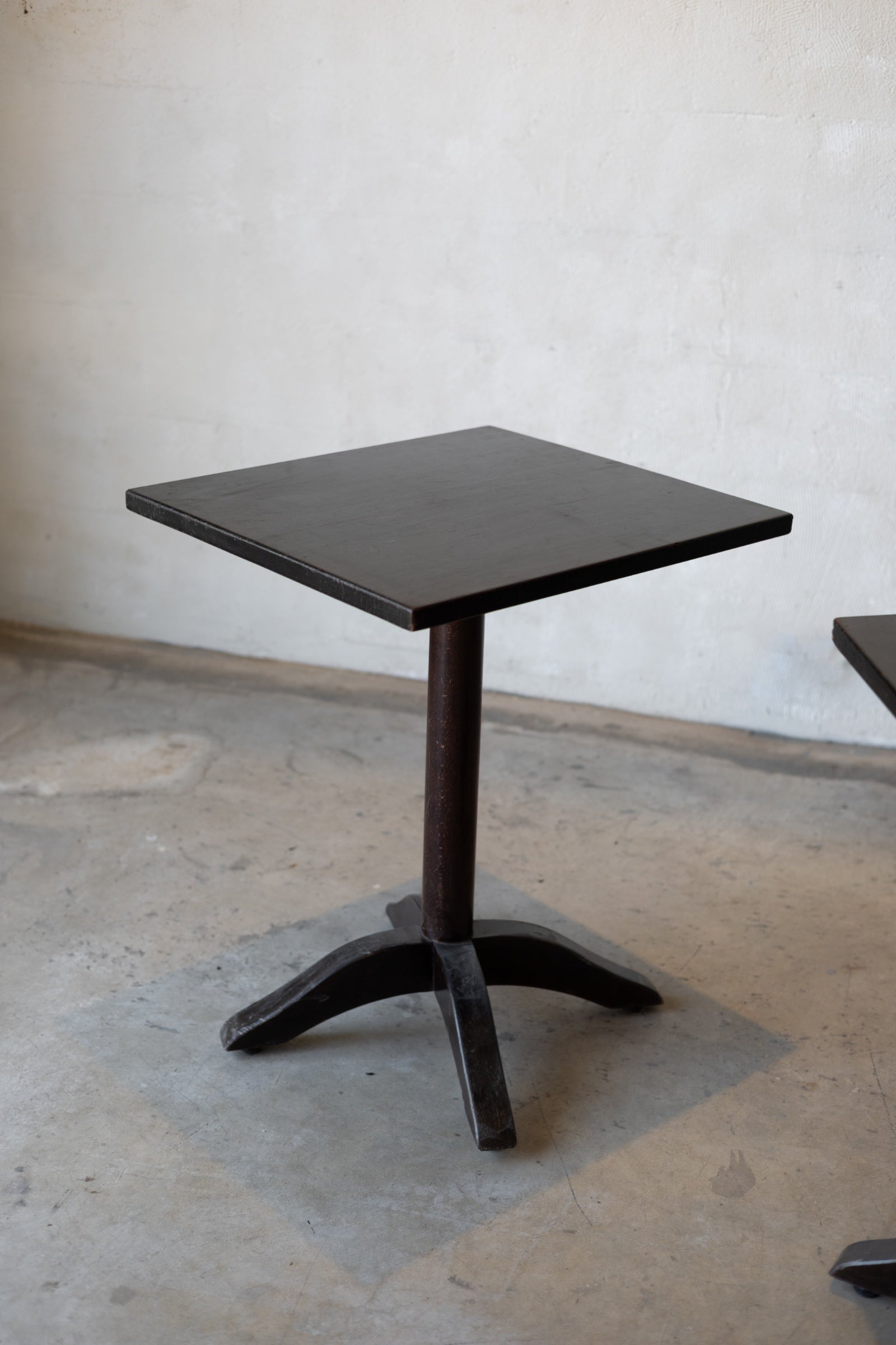 Small black bistro table with a single pedestal base on a concrete floor against a plain wall.