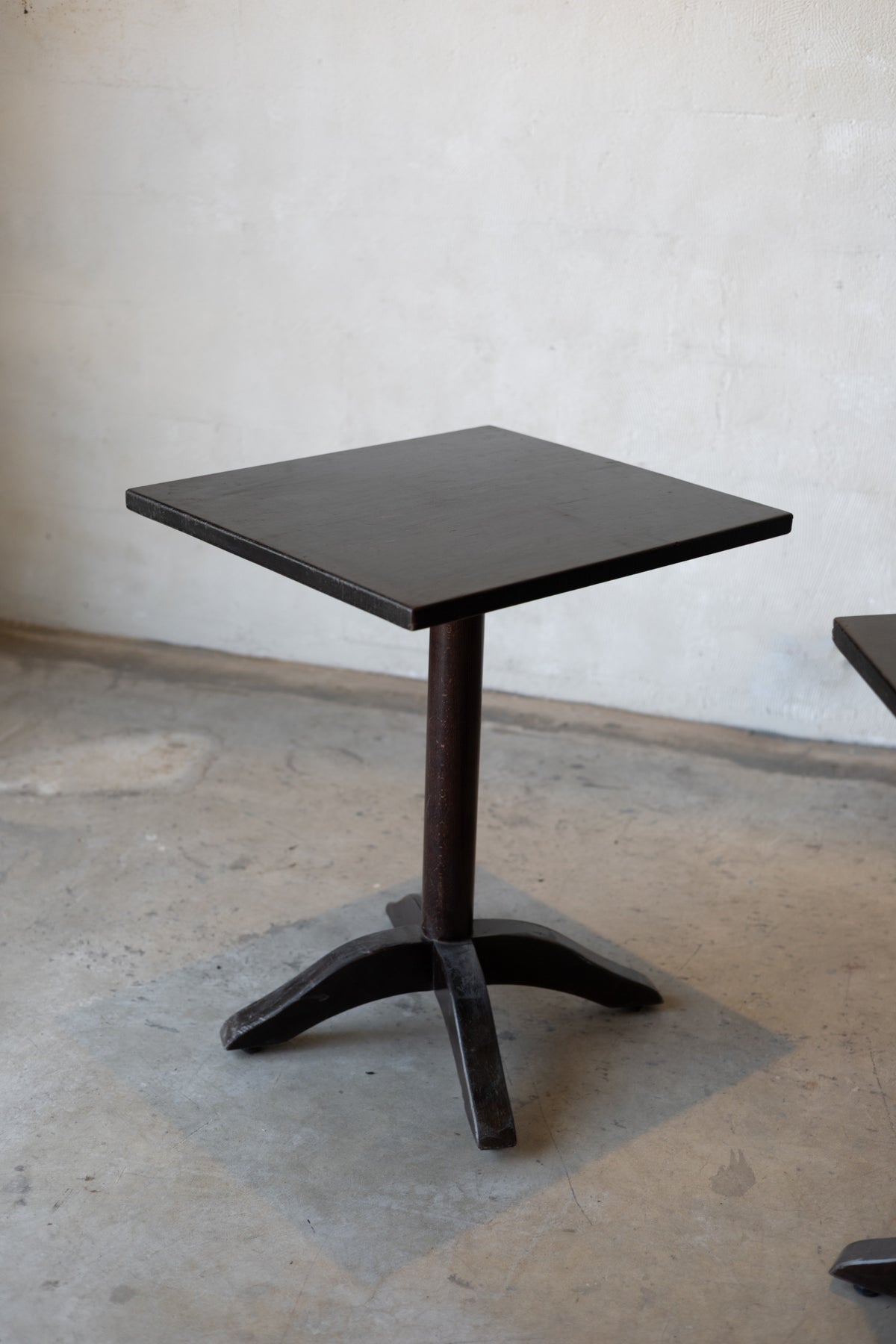 Small black bistro table with a single pedestal base on a concrete floor against a plain wall.