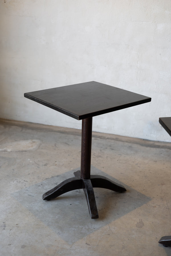 Small black bistro table with a single pedestal base on a concrete floor against a plain wall.