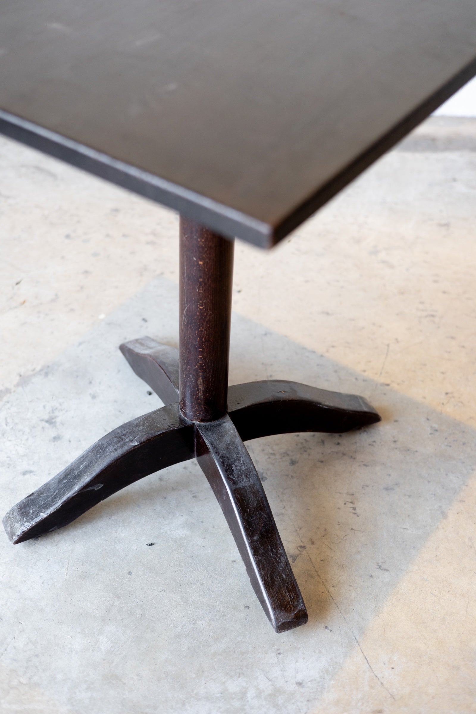 Dark wood table with a unique pedestal base design on a light floor.
