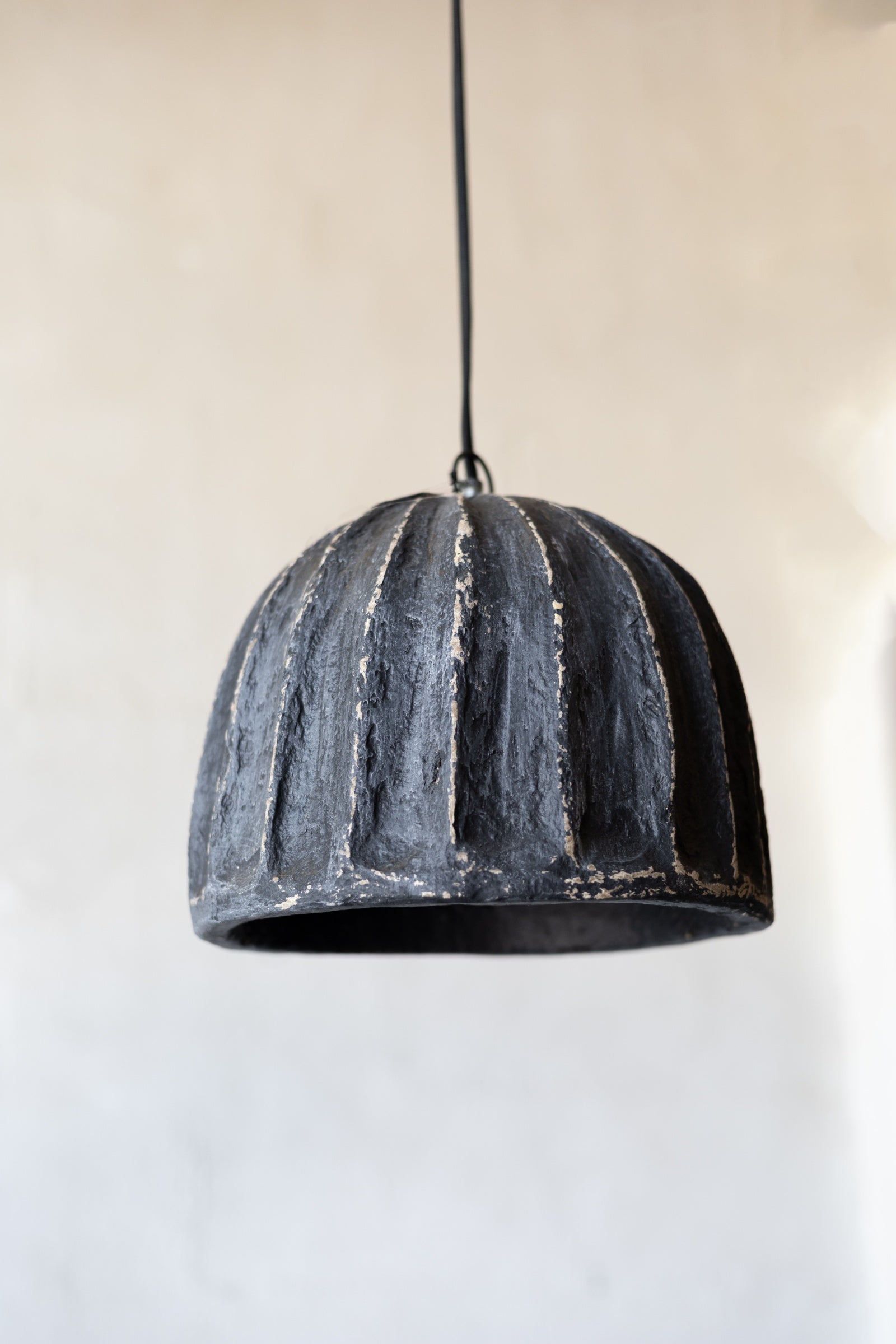 Black textured pendant light against a neutral background.