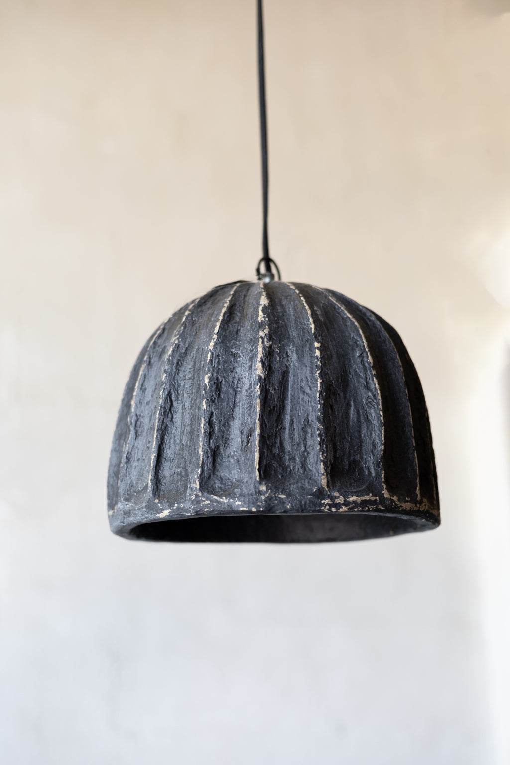 Black textured pendant light against a neutral background.