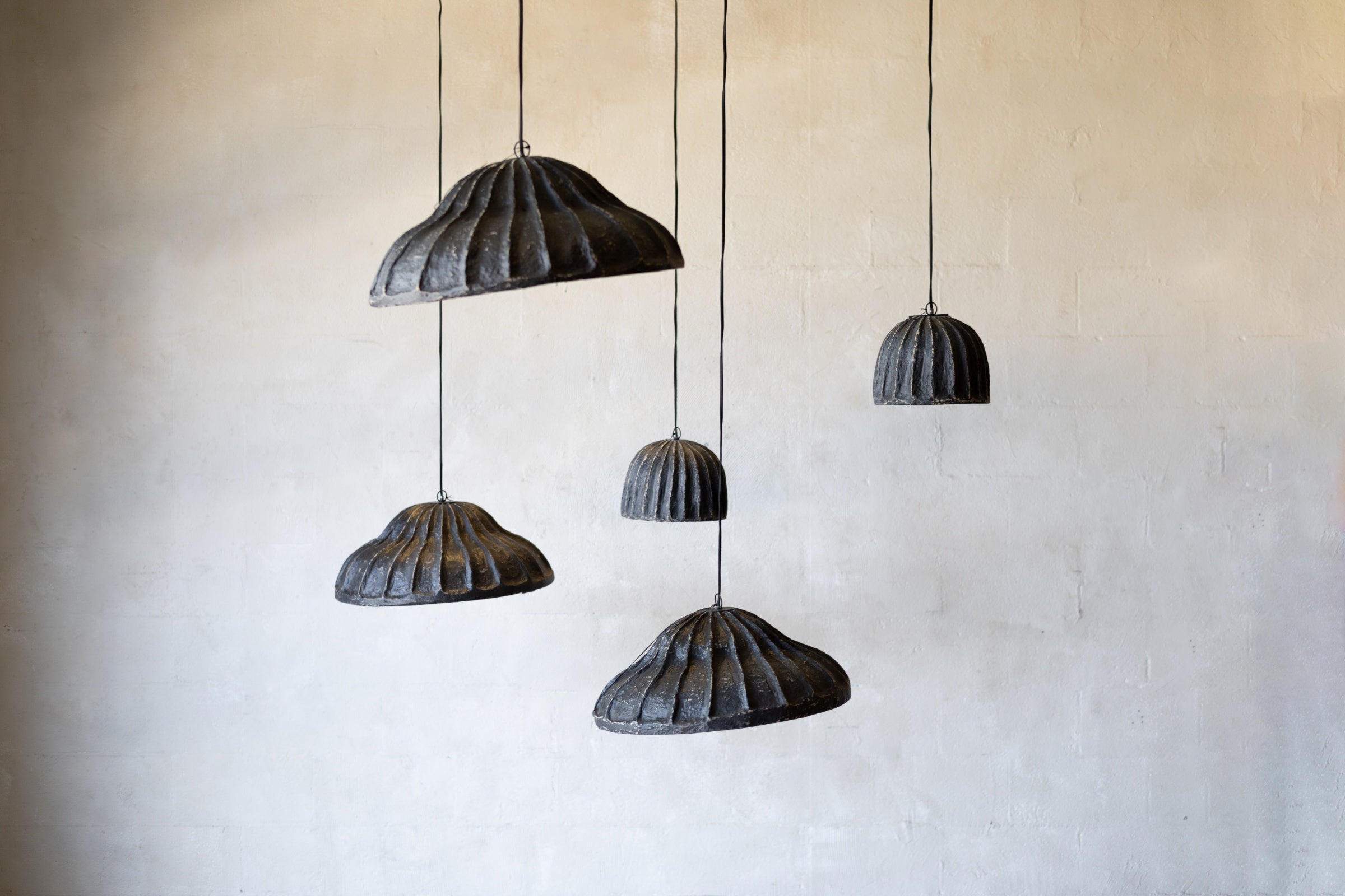 Set of five black pendant lights hanging against a beige wall.