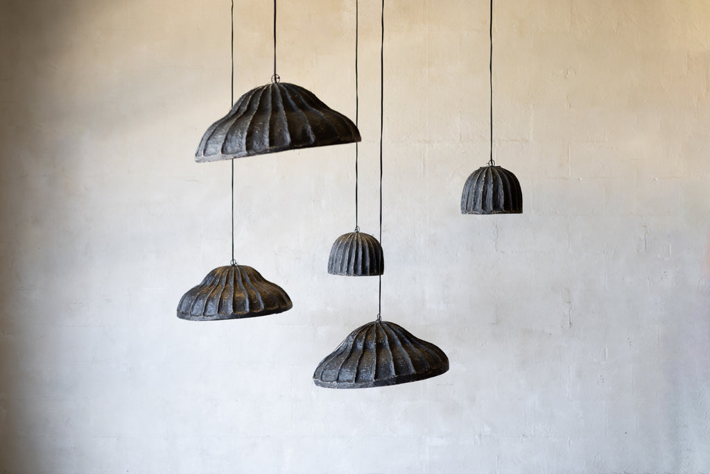 Set of five black pendant lights hanging against a beige wall.