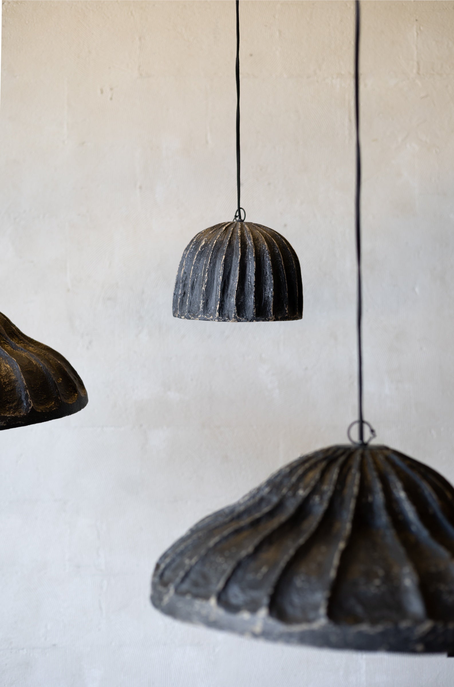 Three rustic papier mache pendant lights hanging against a plain wall.