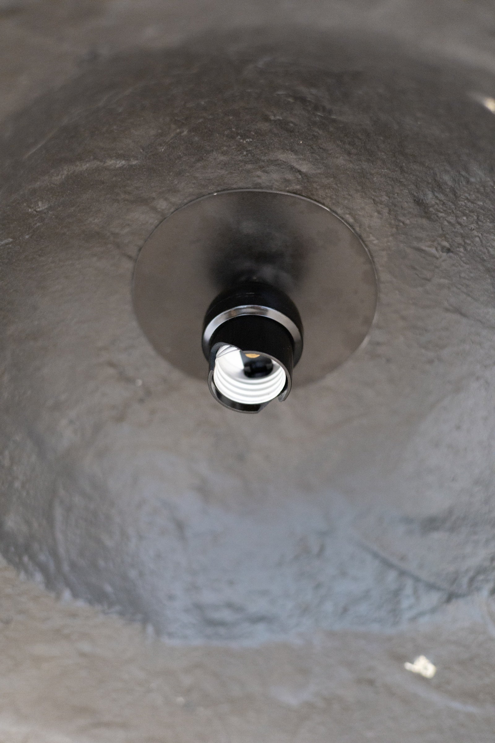 Close-up of a light bulb socket inside a textured black pendant light. 