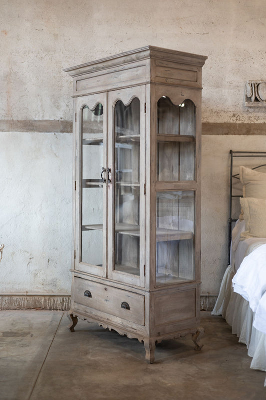 Vintage-style wooden cabinet with glass doors in a bedroom setting.