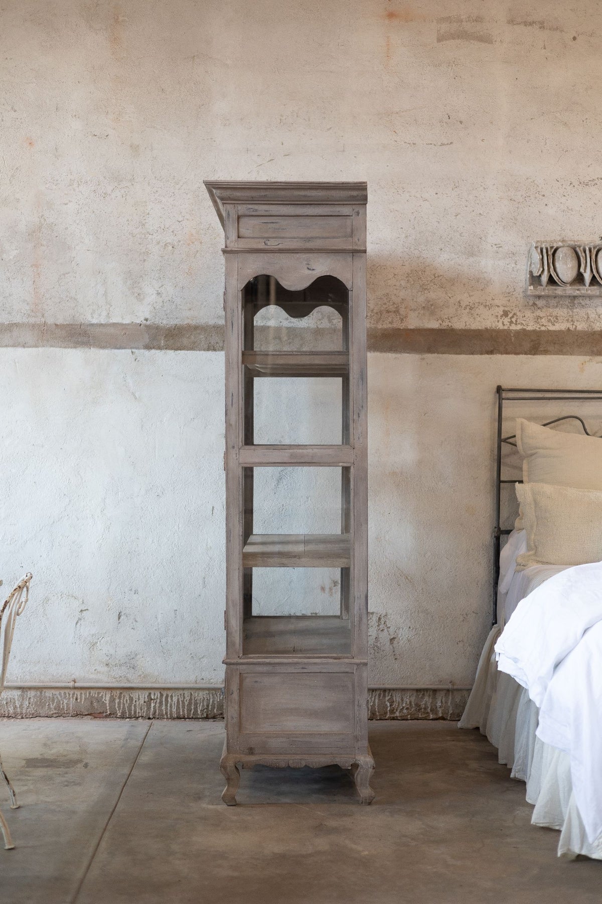 Side of wooden and glass cabinet against a textured wall in a room.