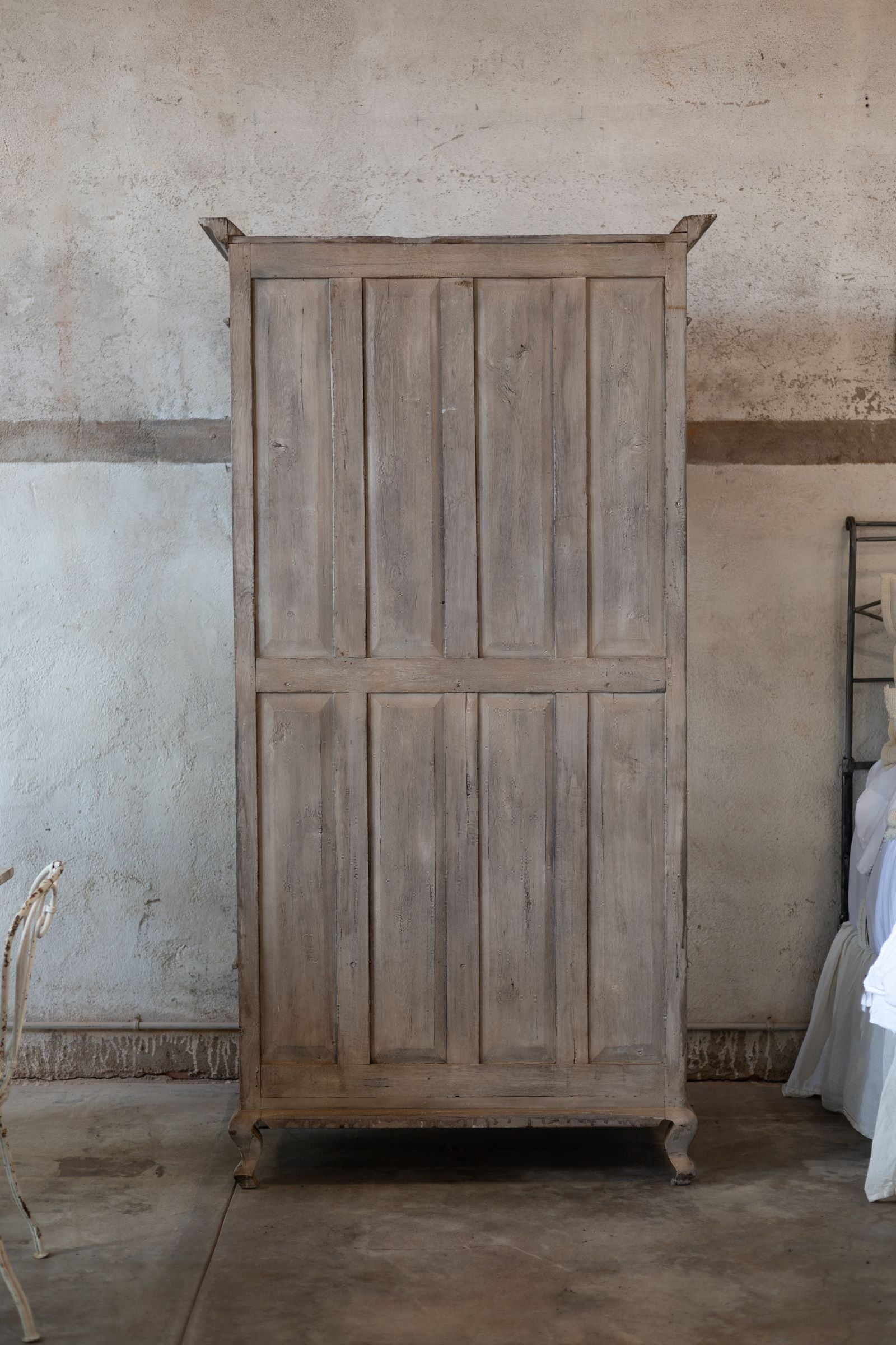 Back of wooden cabinet against a textured wall in a room with a bed and chair.